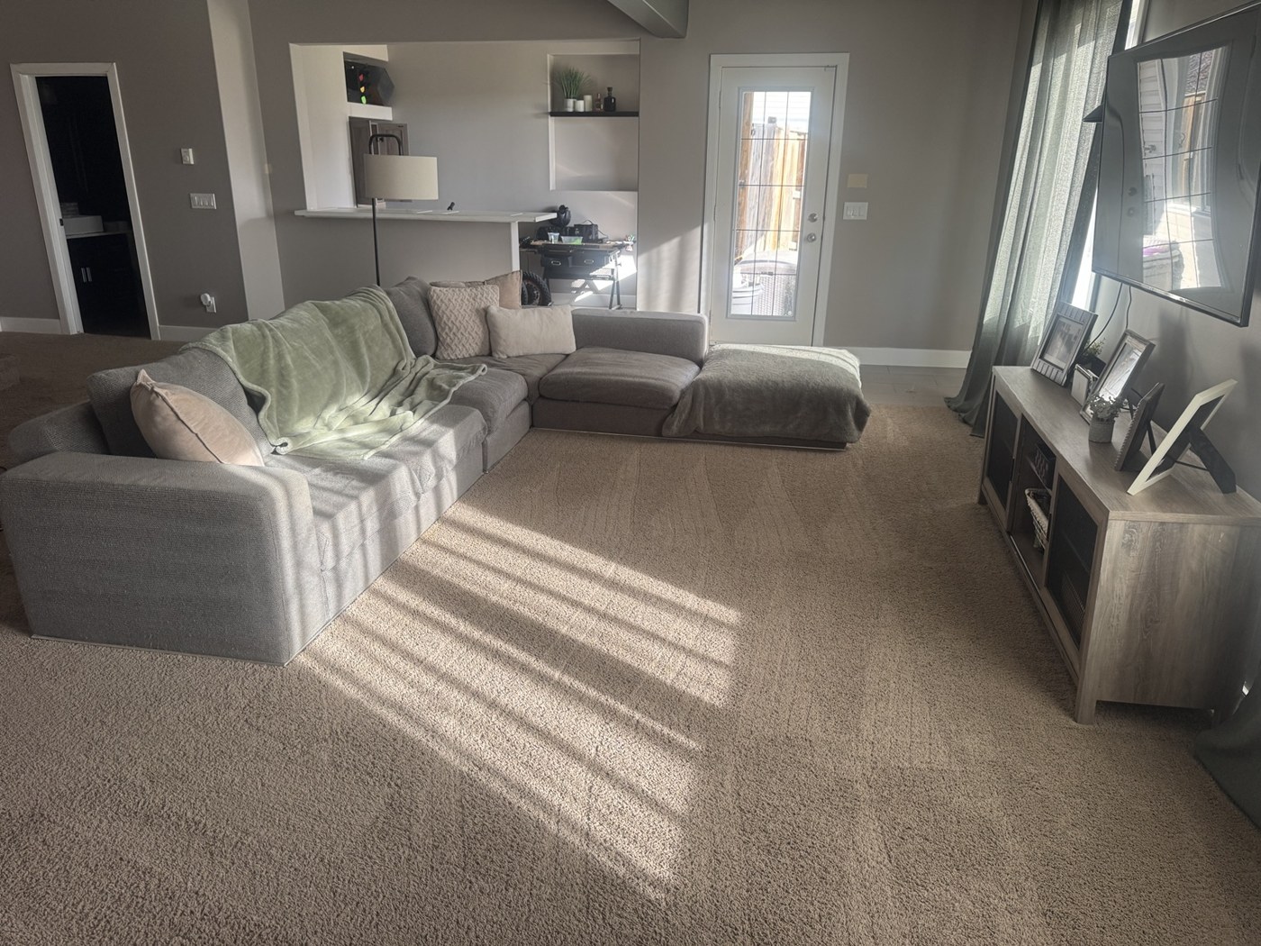 Living area after cleaning, with a clear carpeted floor and neatly arranged sofa cushions and throws